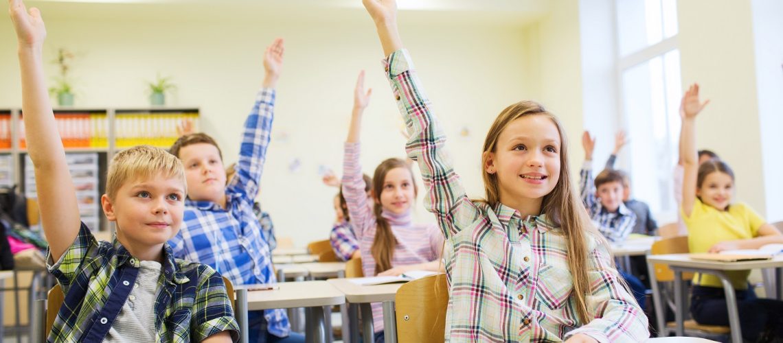 education, elementary school, learning and people concept - group of school kids with notebooks sitting in classroom and raising hands